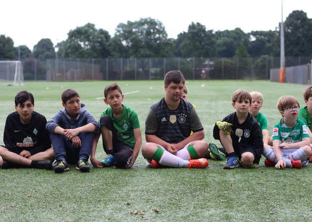 verschiedene Kinder sitzen auf einem Fußballfeld