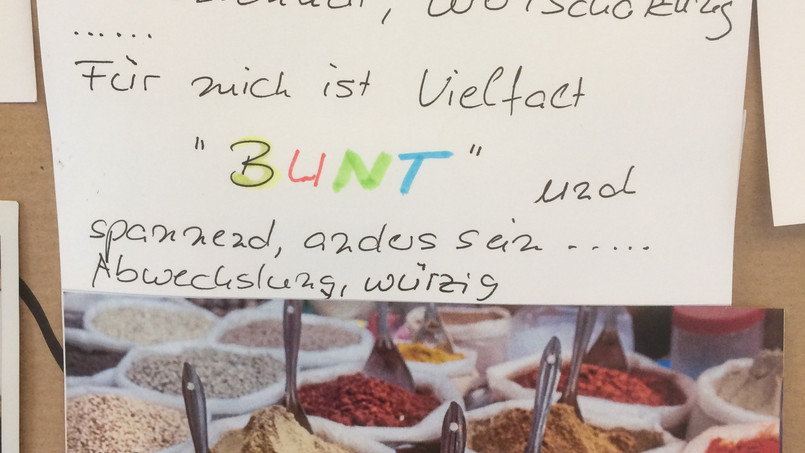 Ein Schild zur Bedeutung von Diversity und ein Bild mit Gewürzen hängt an einem Brett.