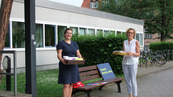 Zwei Frauen stehen an einer Bank und tragen Serviertabletts mit Postkarten.