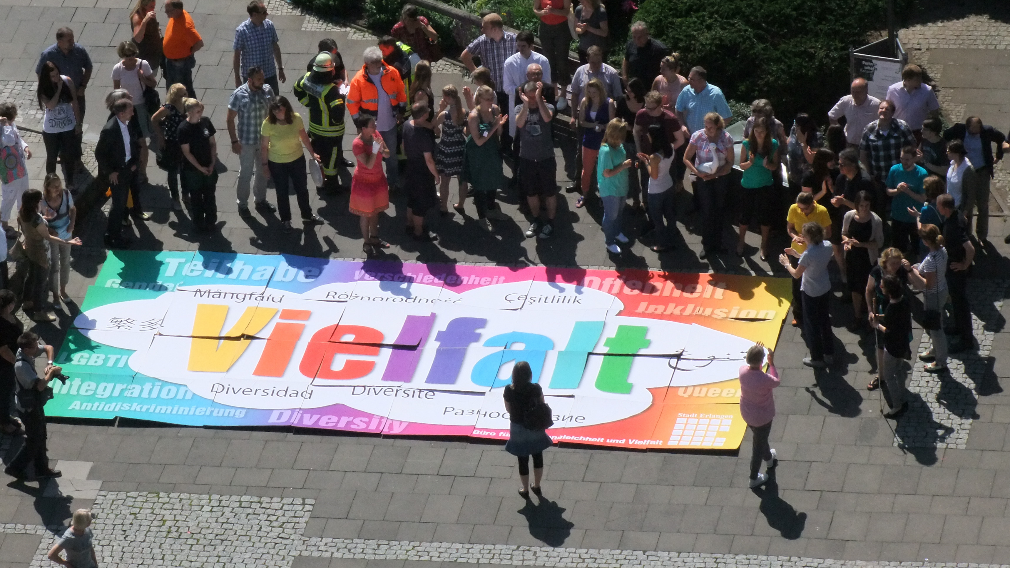 Große Gruppe Menschen steht um ein großes Puzzle mit der Aufschrift Vielfalt herum.