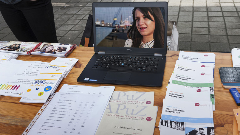 Auf dem Tisch stehen stehen mehrere Infobroschüren und Flyer und ein Laptop, auf dem ein Film abgespielt wird.