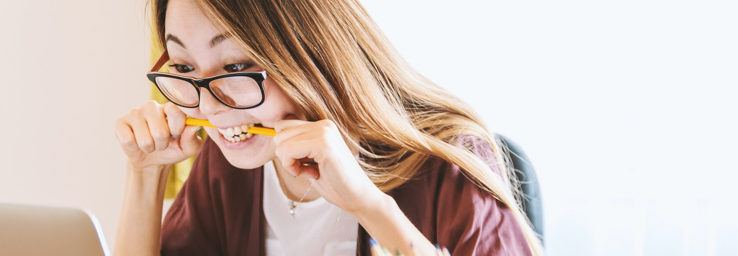 Frau vor dem Computer sitzend und einen Stift im Mund