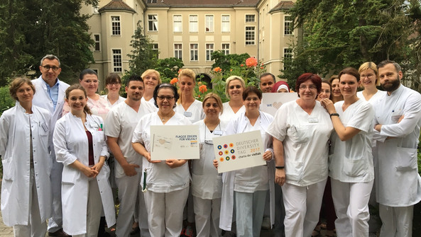 Mitarbeitende des Jüdischen Krankenhauses stehen zusammen und halten das Logo und die Flagge der Charta der Vielfalt. 